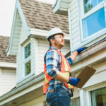 man with hard hat standing on steps inspecting house roof